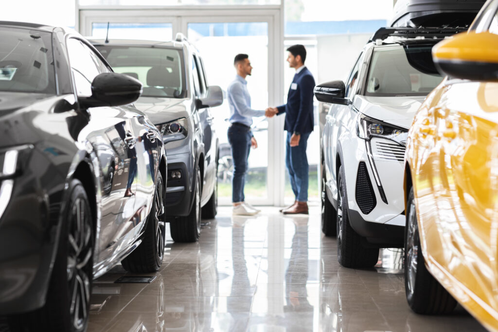 Customer and sales assistant shaking hands, car showroom interior