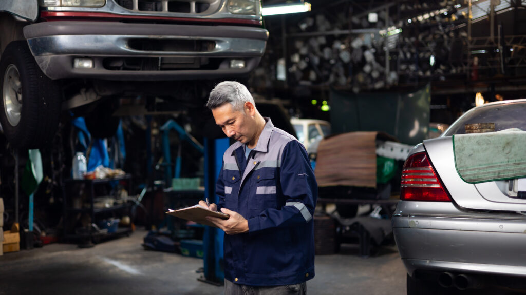 Accident Inspector Inspect damage car caused by car crash on the road. Car insurance agent examining white car by digital tablet in garage.